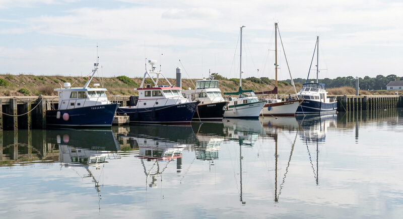 Several charter boats of different sizes moored side by side in a tidal harbor at high water, reflections on still water.